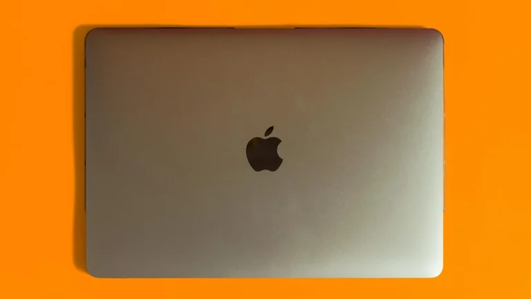 A closed silver MacBook placed against a vibrant orange backdrop.
