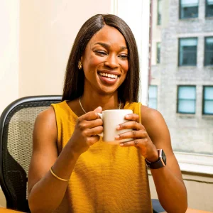 Smiling woman in mustard color top holding a mug