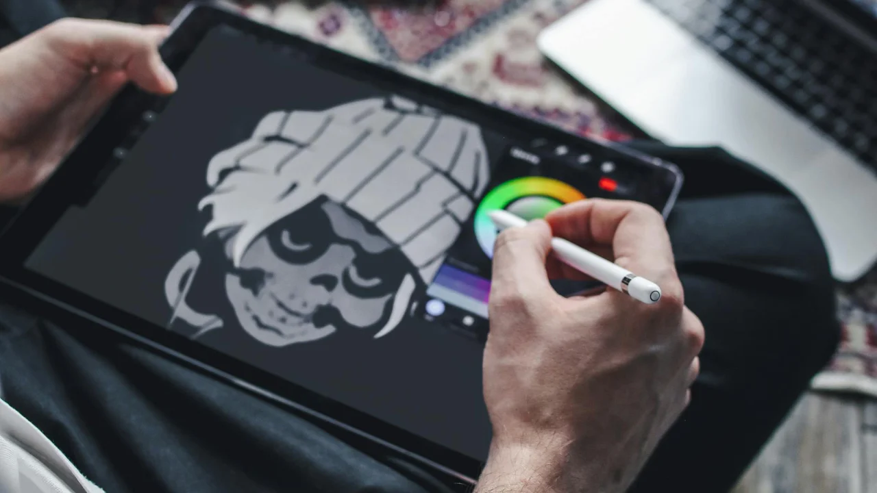 A person using a stylus to draw a stylised skull with a beanie on a digital tablet.